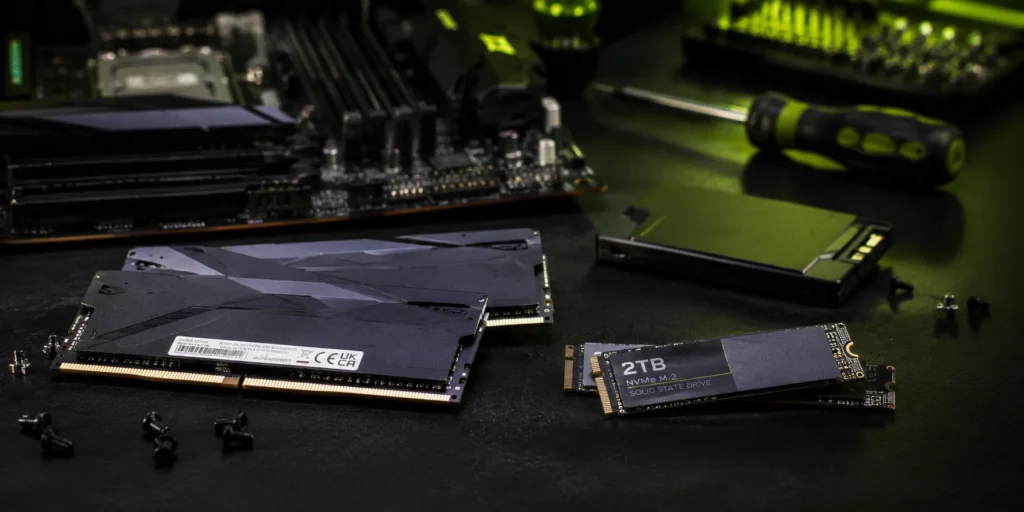 RAM-minnepinner og en 2TB NVMe M.2 SSD plassert foran et hovedkort med skruer og skrutrekker