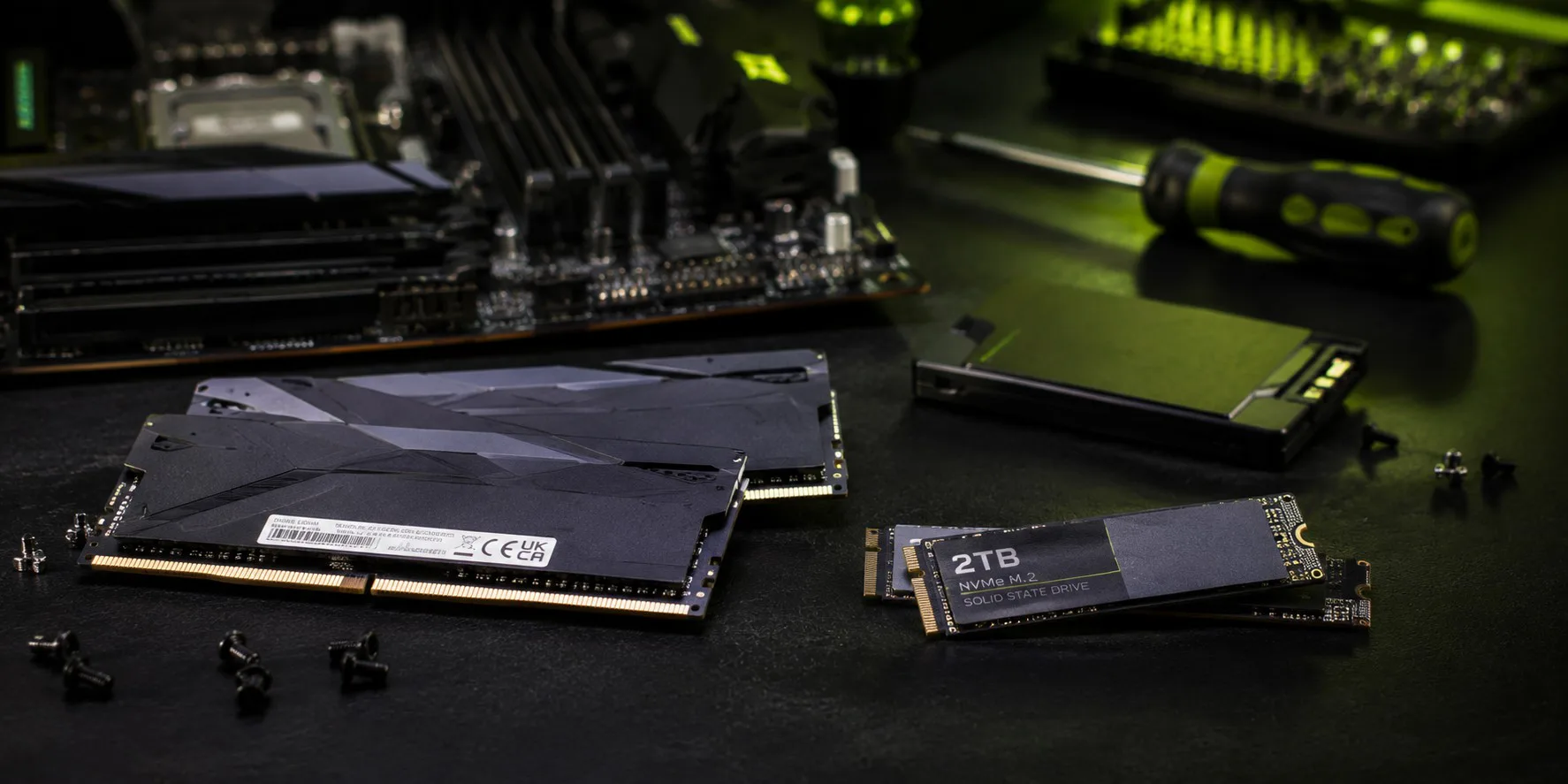 RAM-minnepinner og en 2TB NVMe M.2 SSD plassert foran et hovedkort med skruer og skrutrekker
